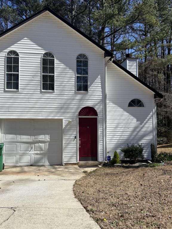 traditional-style house featuring an attached garage, a chimney, and concrete driveway