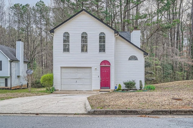 traditional home with concrete driveway, a forest view, a garage, and a chimney