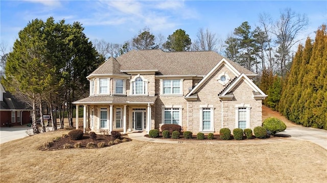 view of front facade with brick siding, roof with shingles, and a front yard