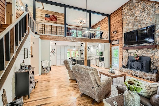 living room featuring a wood stove, light wood-style floors, a high ceiling, wooden walls, and a ceiling fan