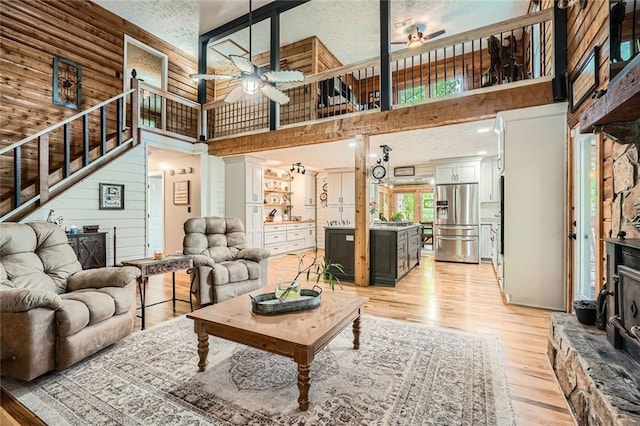 living area featuring light wood-style floors, a towering ceiling, ceiling fan, and stairs