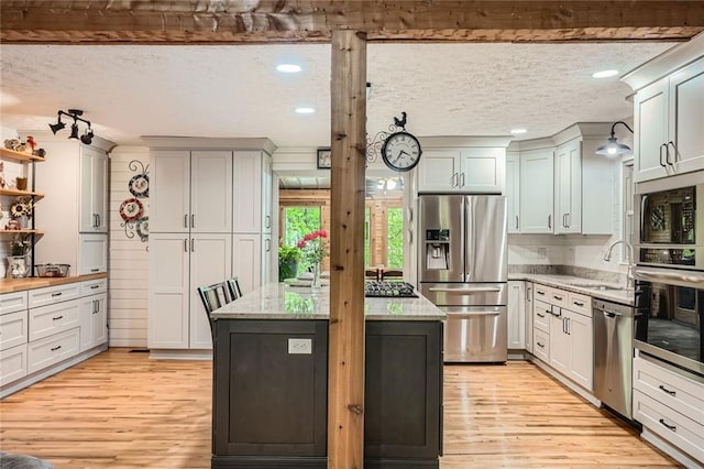 kitchen featuring light stone countertops, a sink, light wood finished floors, stainless steel appliances, and a kitchen island