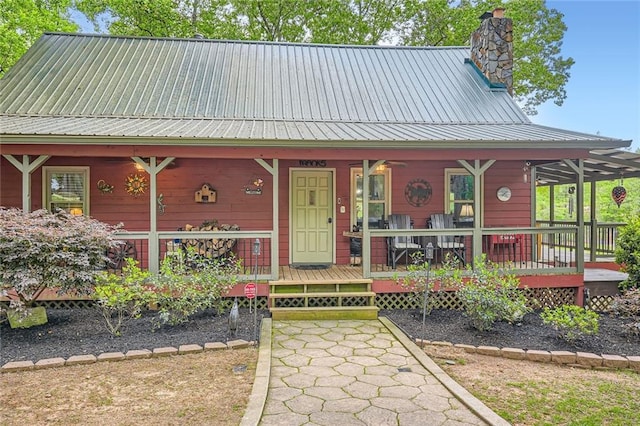 view of front facade with covered porch, a chimney, and metal roof