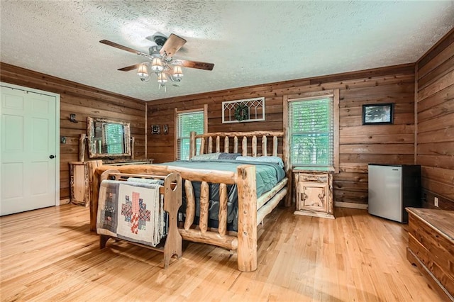 bedroom with freestanding refrigerator, wooden walls, a textured ceiling, and hardwood / wood-style flooring