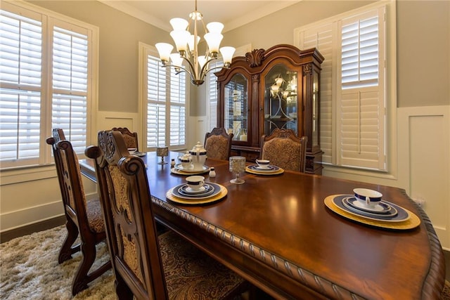 dining space featuring a chandelier, a decorative wall, a wainscoted wall, and ornamental molding