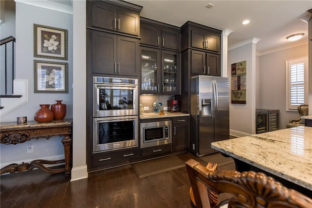 kitchen with ornamental molding, light stone counters, appliances with stainless steel finishes, and dark wood finished floors