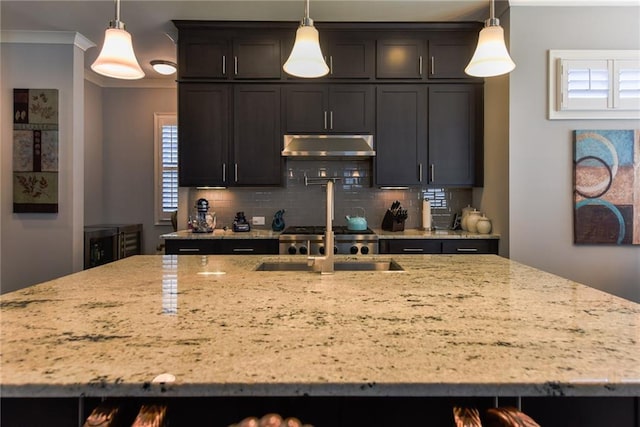 kitchen with light stone countertops, a kitchen island with sink, under cabinet range hood, and backsplash