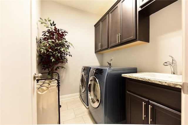 clothes washing area featuring washing machine and clothes dryer, a sink, light tile patterned floors, cabinet space, and baseboards