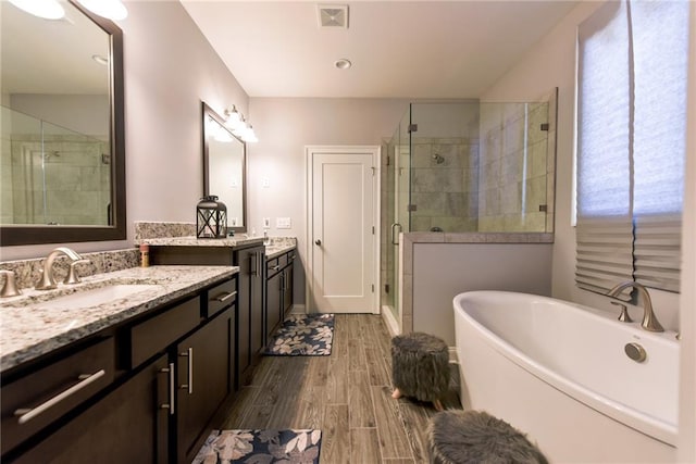 full bathroom featuring a sink, wood tiled floor, a stall shower, a freestanding tub, and visible vents