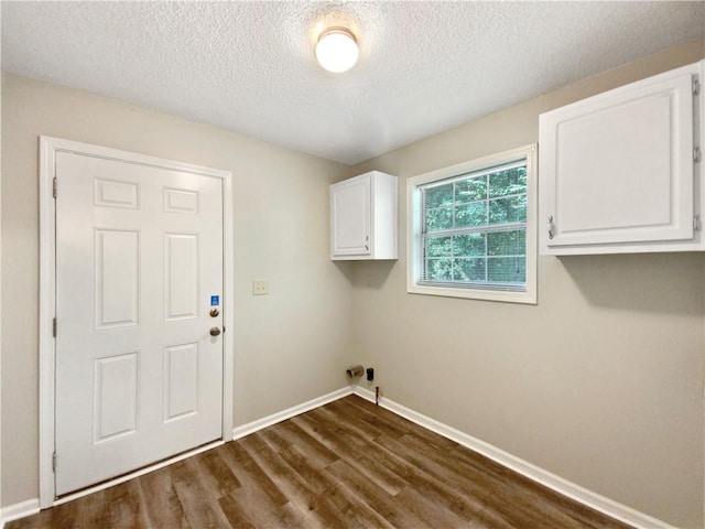 clothes washing area with a textured ceiling, dark wood-type flooring, and cabinets