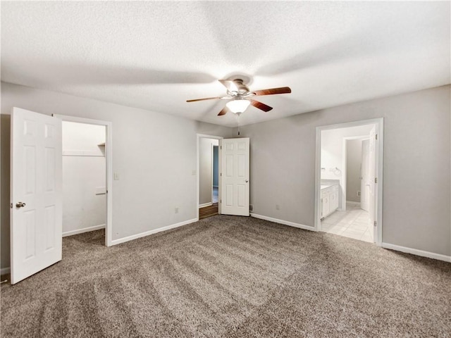 unfurnished bedroom with a textured ceiling, a walk in closet, baseboards, and carpet floors