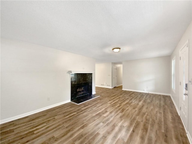 unfurnished living room with wood finished floors, baseboards, a high end fireplace, and a textured ceiling