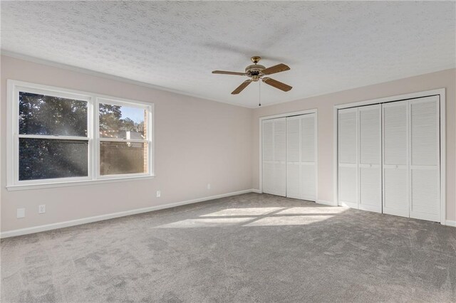 unfurnished bedroom with ceiling fan, two closets, a textured ceiling, and carpet