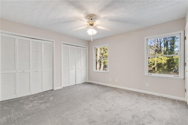 unfurnished bedroom with ceiling fan, light carpet, two closets, and a textured ceiling