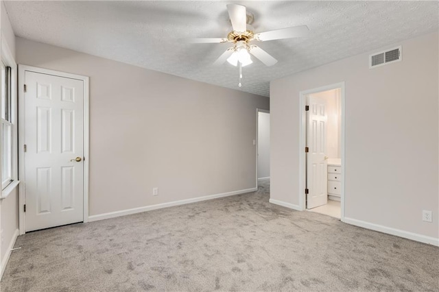 unfurnished bedroom with ceiling fan, light colored carpet, ensuite bathroom, and a textured ceiling