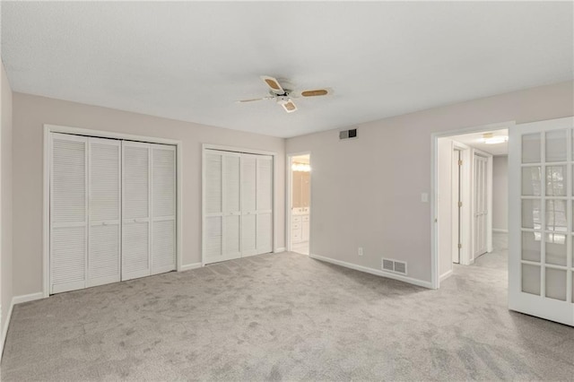 unfurnished bedroom featuring ceiling fan, light colored carpet, connected bathroom, and two closets