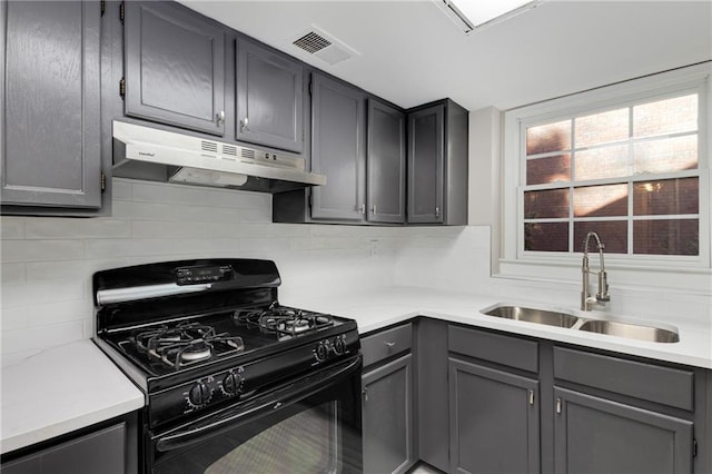 kitchen featuring sink, black range with gas stovetop, gray cabinets, and backsplash