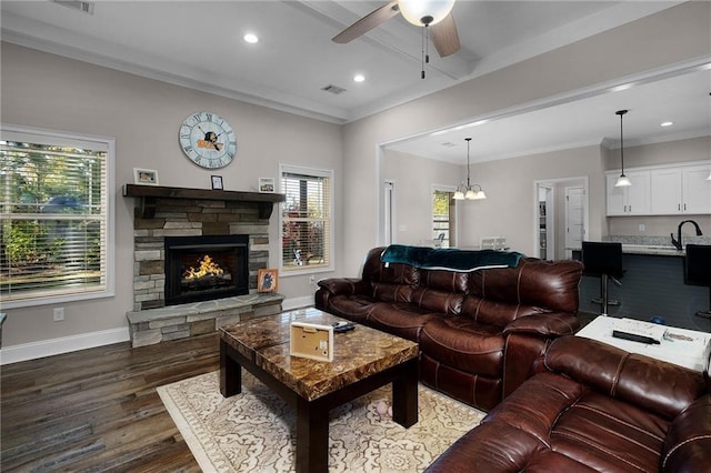 living room with ceiling fan with notable chandelier, a fireplace, sink, dark hardwood / wood-style flooring, and crown molding