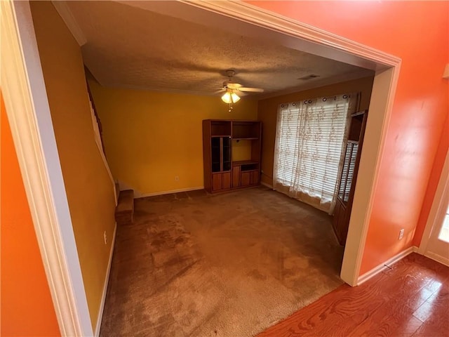 unfurnished living room with dark carpet, crown molding, ceiling fan, and a textured ceiling