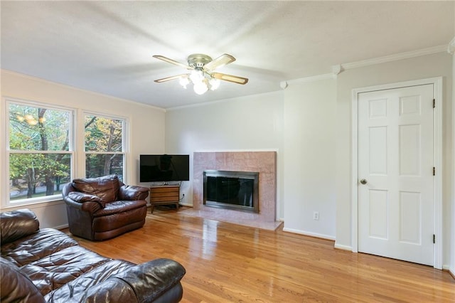 living room with ceiling fan, wood-type flooring, a tile fireplace, and crown molding