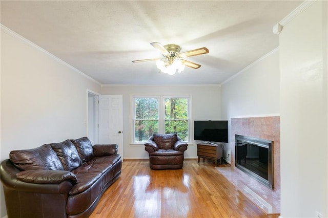 living room featuring crown molding, wood-type flooring, a tiled fireplace, and ceiling fan