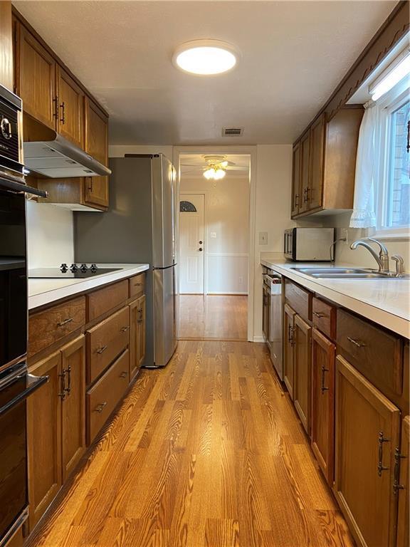 kitchen with black appliances, ceiling fan, sink, and light hardwood / wood-style flooring