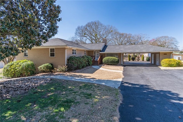 ranch-style home featuring a carport, aphalt driveway, a chimney, and brick siding