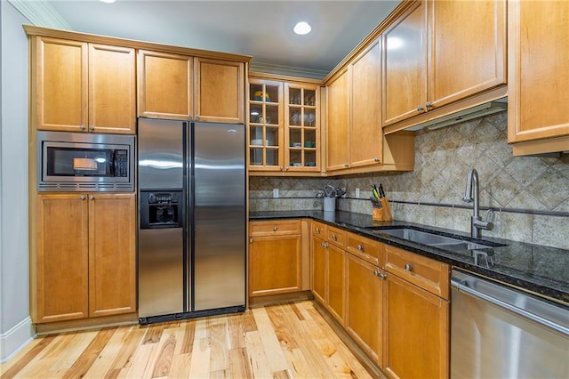 kitchen featuring light wood finished floors, decorative backsplash, dark stone counters, appliances with stainless steel finishes, and a sink