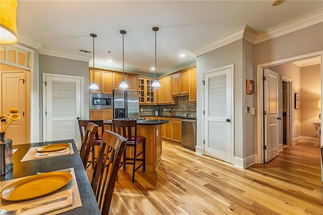 kitchen featuring brown cabinetry, dark countertops, a kitchen island, appliances with stainless steel finishes, and light wood-type flooring