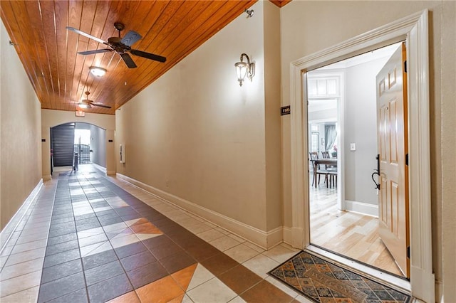 hallway with arched walkways, wooden ceiling, baseboards, and tile patterned floors