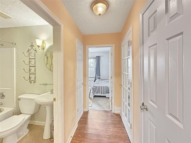 full bathroom with shower / bathing tub combination, sink, hardwood / wood-style flooring, toilet, and a textured ceiling