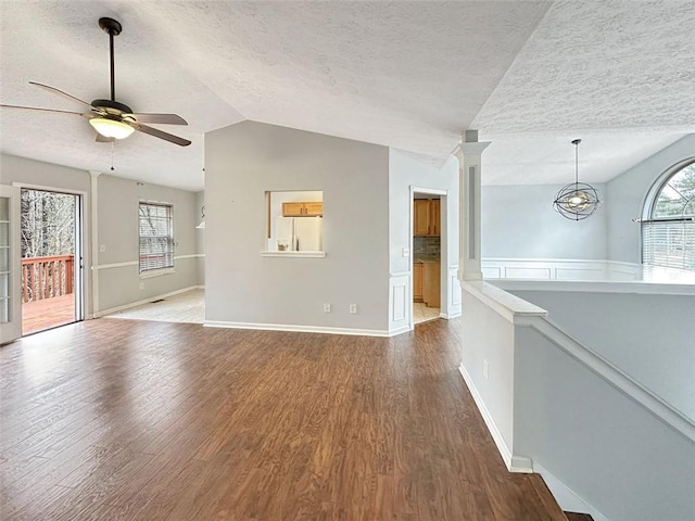 unfurnished living room featuring a textured ceiling, ceiling fan with notable chandelier, lofted ceiling, and hardwood / wood-style flooring