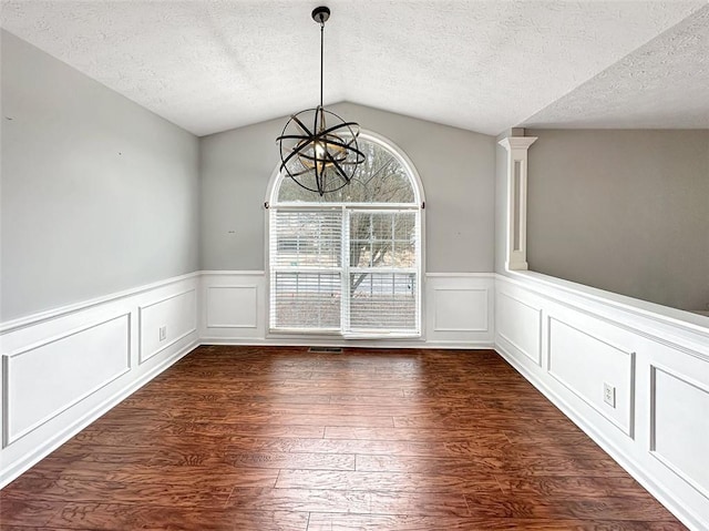 unfurnished dining area featuring a textured ceiling, dark wood-type flooring, a chandelier, and vaulted ceiling