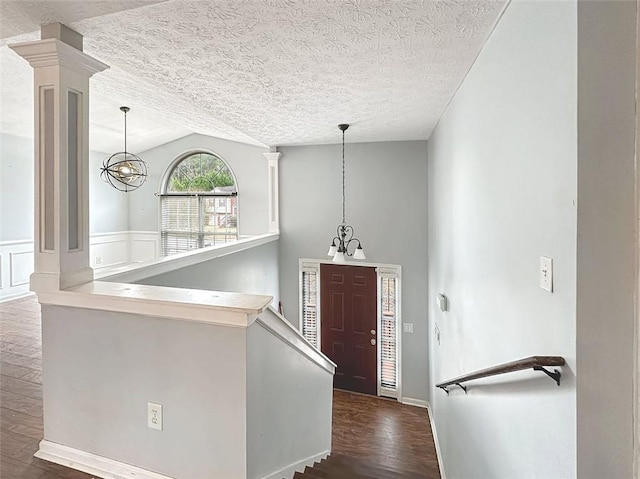 entrance foyer featuring decorative columns, a textured ceiling, a chandelier, dark hardwood / wood-style floors, and lofted ceiling