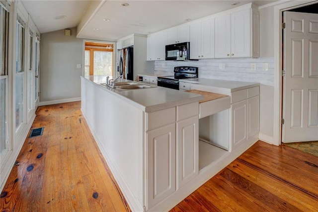 kitchen with an island with sink, black appliances, tasteful backsplash, light wood-type flooring, and white cabinetry