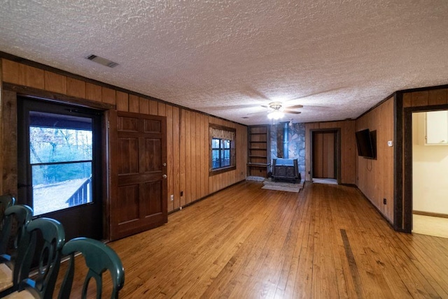 unfurnished living room with crown molding, a wealth of natural light, light hardwood / wood-style floors, a textured ceiling, and a wood stove