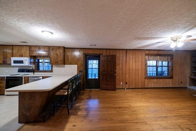 kitchen with a textured ceiling, light wood-type flooring, a kitchen breakfast bar, kitchen peninsula, and white appliances