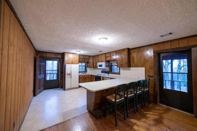 kitchen with wood walls, a breakfast bar area, light hardwood / wood-style floors, kitchen peninsula, and white appliances