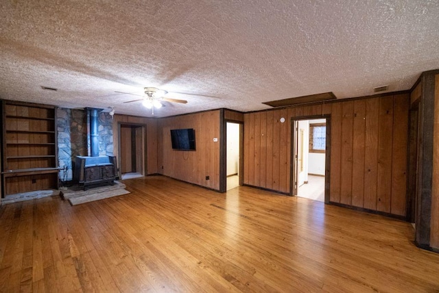 unfurnished living room featuring light hardwood / wood-style flooring, built in features, ceiling fan, a textured ceiling, and a wood stove