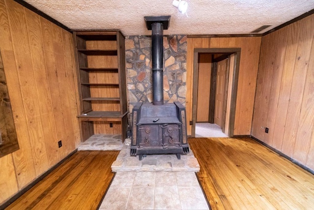 living room featuring light hardwood / wood-style flooring, wood walls, a textured ceiling, and a wood stove