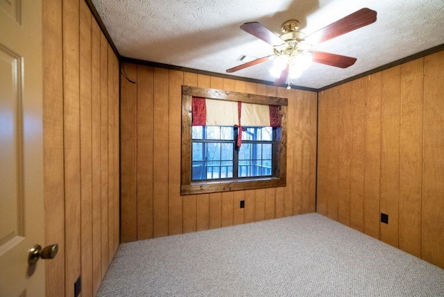 empty room featuring a textured ceiling, ornamental molding, wooden walls, ceiling fan, and carpet