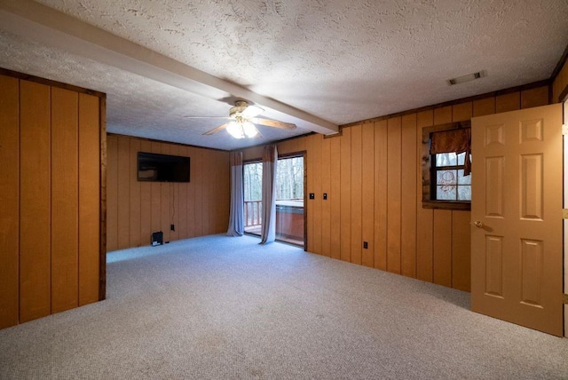 empty room with light colored carpet, a textured ceiling, wooden walls, beamed ceiling, and ceiling fan