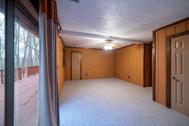 empty room with ceiling fan, carpet flooring, a textured ceiling, and wood walls