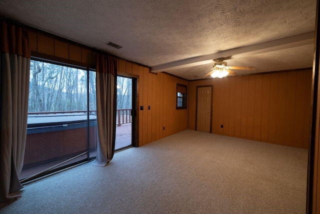 empty room with wood walls, a textured ceiling, ceiling fan, beam ceiling, and carpet