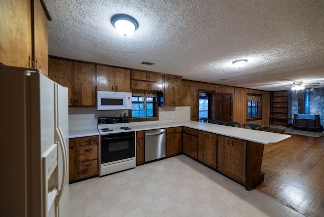 kitchen featuring white appliances, a kitchen breakfast bar, a textured ceiling, kitchen peninsula, and a wood stove