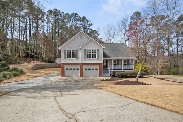 split level home featuring a chimney, a porch, concrete driveway, and a garage