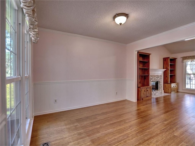 unfurnished living room featuring a stone fireplace, wainscoting, a textured ceiling, and wood finished floors