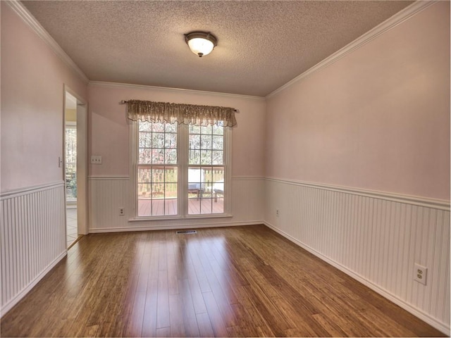 empty room featuring a textured ceiling, wood finished floors, wainscoting, and ornamental molding