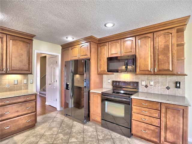 kitchen with brown cabinets, black appliances, light stone counters, tasteful backsplash, and light tile patterned floors