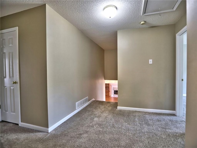 empty room featuring visible vents, carpet flooring, a fireplace, and attic access